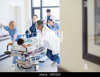 Doctors and nurses rushing patient on stretcher down hospital corridor Stock Photo