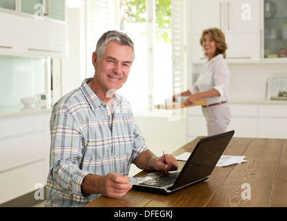Portrait of smiling senior man using laptop in kitchen Stock Photo
