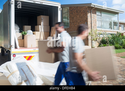 Movers carrying cardboard boxes in driveway Stock Photo