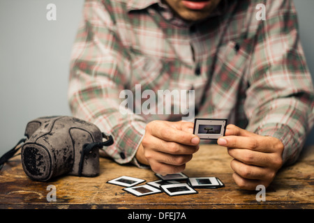 Young photographer is sitting at a table and looking over his old slides Stock Photo