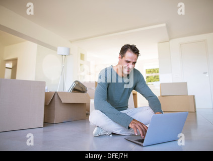 Man using laptop on floor among cardboard boxes Stock Photo