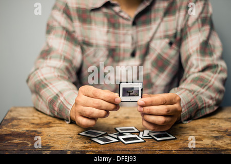 Young man is sitting at a table and looking over his old slides Stock Photo
