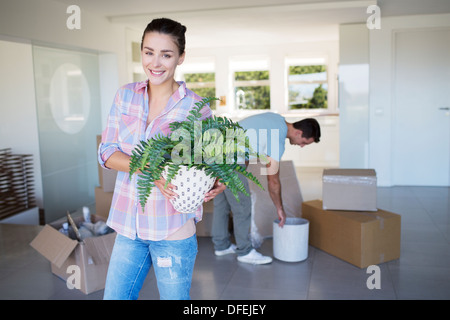 Portrait of smiling woman holding potted plant in new house
