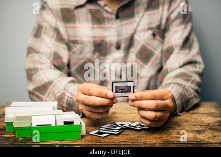 Young man is sitting at a table and looking over his old slides Stock Photo