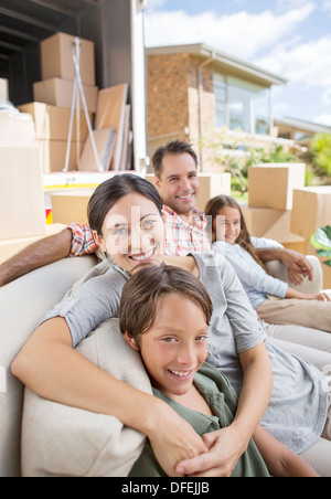 Family sitting on sofa near moving van in driveway Stock Photo