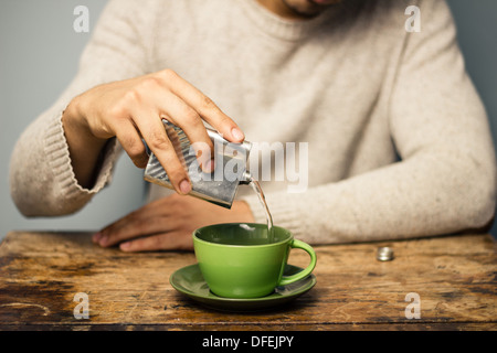 Young man at table in cafe is making his coffee irish by adding alcohol from a flask Stock Photo