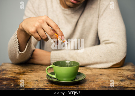 Young man at table in cafe is adding sugar to his coffee Stock Photo