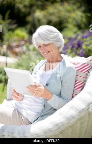 Senior woman using digital tablet in armchair Stock Photo