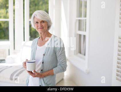 Senior woman holding cup of coffee in sun room Stock Photo
