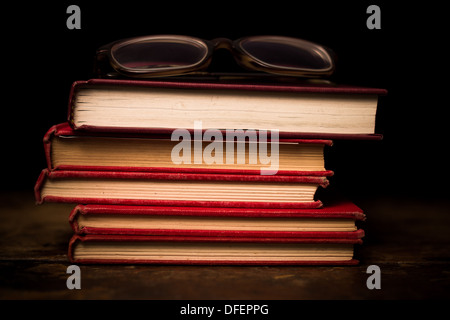 Stack of red books on wood surface with pair of glasses Stock Photo