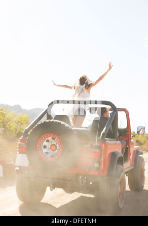 Woman cheering in sport utility vehicle on dirt road Stock Photo