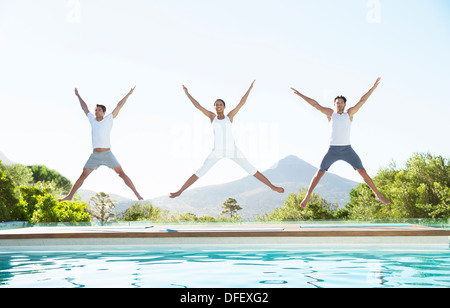 People jumping with arms and legs outstretched at poolside Stock Photo
