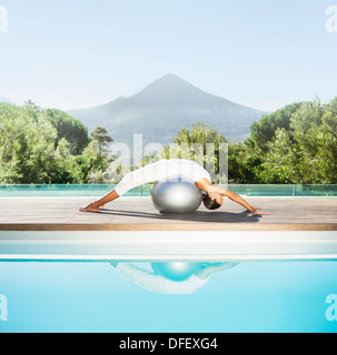 Woman stretching over fitness ball at poolside Stock Photo