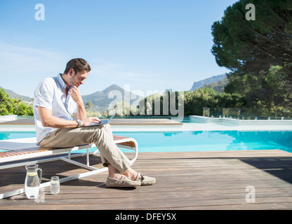 Man using laptop at poolside Stock Photo