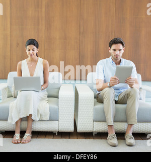 Couple using digital tablet and laptop in armchairs Stock Photo