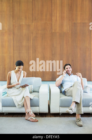 Couple using laptop and cell phone in armchairs Stock Photo