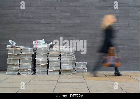 Woman walks past stacks of free Metro newspaper during morning rush hour in Manchester. Stock Photo