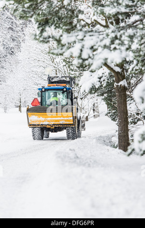 Winter forest with maintenance truck plowing and sanding an icy road Stock Photo