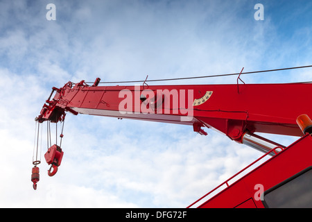 Red truck crane boom with hooks and scale weight above blue sky Stock Photo