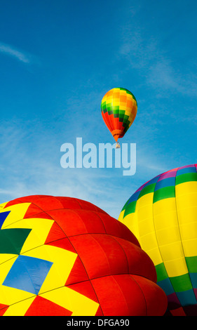 A colorful hot air balloon flies in a bright blue sky as two more are inflated on the ground. Stock Photo