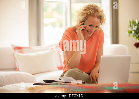 Woman talking on cell phone and using laptop in living room Stock Photo