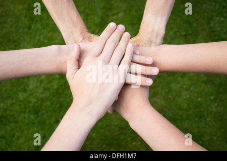 Six arms on top of each other uniting above grass Stock Photo