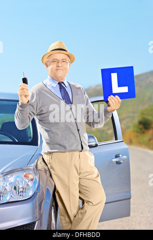 Smiling mature man on his car holding a L sign and car key after having his driver's license Stock Photo