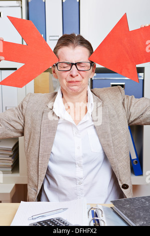 Business woman in office with headache pointing to head with red arrows Stock Photo