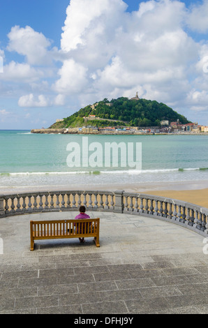 Woman seated on a bench on the Promenade La Concha overlooking the beach and Monte Urgull, San Sebastian, Spain Stock Photo