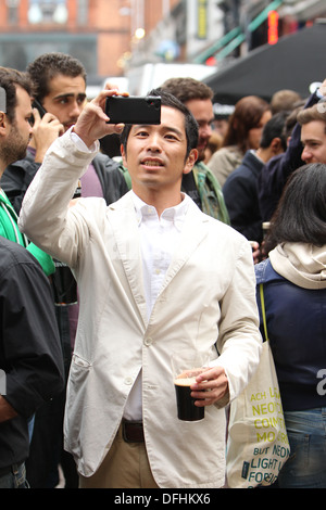 A tourist with a pint of Guinness takes a photo during the Arthur's Day celebrations in Dublin city centre. Stock Photo
