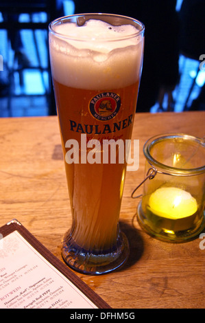 A printed glass of Paulaner beer on a bar in Munich, Bavaria, Germany pub table drinks glasses Stock Photo