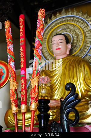 Colourful decorated candles in front of a sitting Buddha at a Buddhist temple in a Vietnamese village. Stock Photo