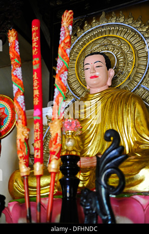 Colourful decorated candles in front of a sitting Buddha at a Buddhist temple in a Vietnamese village. Stock Photo