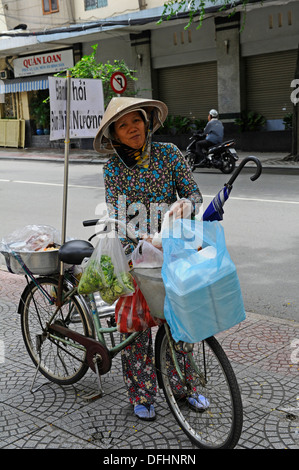 Vietnamese female street trader selling food and snacks from her cycle. Stock Photo