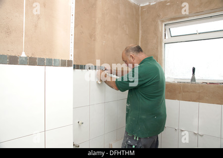 Tiler attaching tiles in a wet room / shower / bathroom on a newly plastered wall Stock Photo