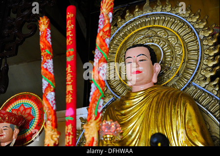 Colourful decorated candles in front of a sitting Buddha at a Buddhist temple in a Vietnamese village. Stock Photo