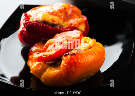 Stuffed bell peppers with chopped meat, cheese and tomato lay on black plate Stock Photo
