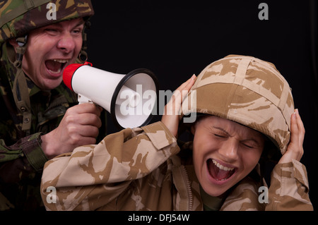 Male soldier shouting orders to a distraught female soldier with the use of a small hand held loudspeaker. British uniforms. Stock Photo