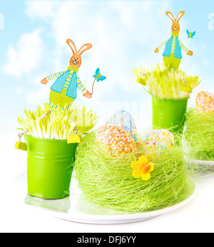 Vivid colorful eggs in green grass nest decorated with cute bunny toys on blue sky background, spring holiday Stock Photo