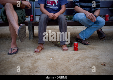Three young men sitting on a bench and drinking beer in Barcelona, Spain. Stock Photo