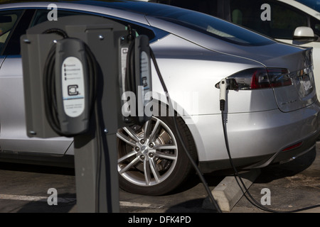 Tesla Model S plug-in electric car plugged into a charging station in a company parking lot. Focus is on the connector plug. Stock Photo