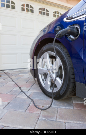 Chevrolet Volt plug-in hybrid electric car with connector plugged in and charging, parked at home in a driveway Stock Photo