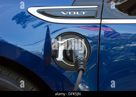 Chevrolet Volt plug-in electric car with connector plugged in and charging with reflection of American flag on vehicle Stock Photo