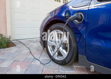 Chevrolet Volt plug-in electric car with connector plugged in charging, at home in a driveway Stock Photo