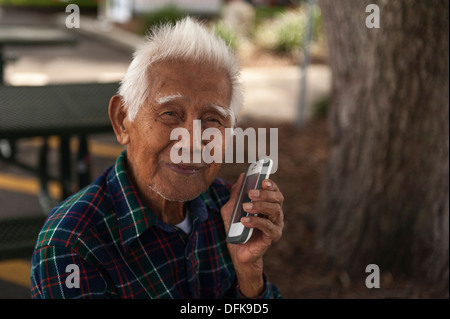 A Senior citizen man with no teeth holding a smart phone close to his face while sitting on a bench at Wooton Park, Tavares FL Stock Photo