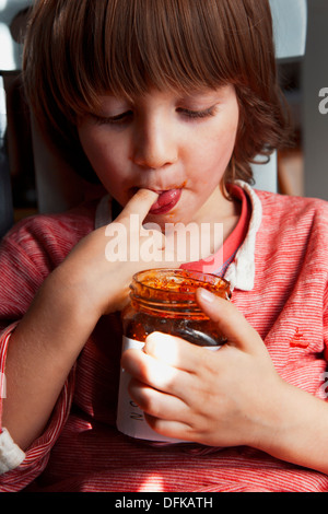 Four and a half year old boy eating fig compote from a jar with his finger. Stock Photo