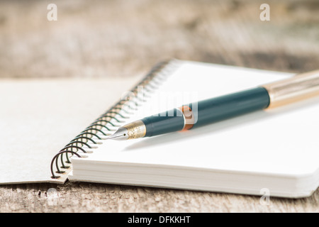 Closeup photo of notebook with old golden ink pen at wood background Stock Photo