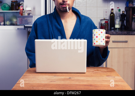 Young man in bathrobe smoking and using laptop Stock Photo