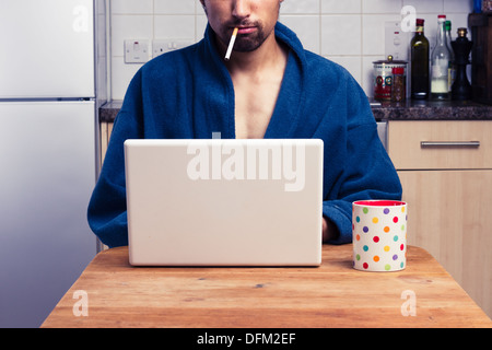Young man in bathrobe using laptop and smoking Stock Photo