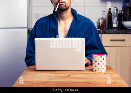 Young man using laptop and smoking in kitchen Stock Photo